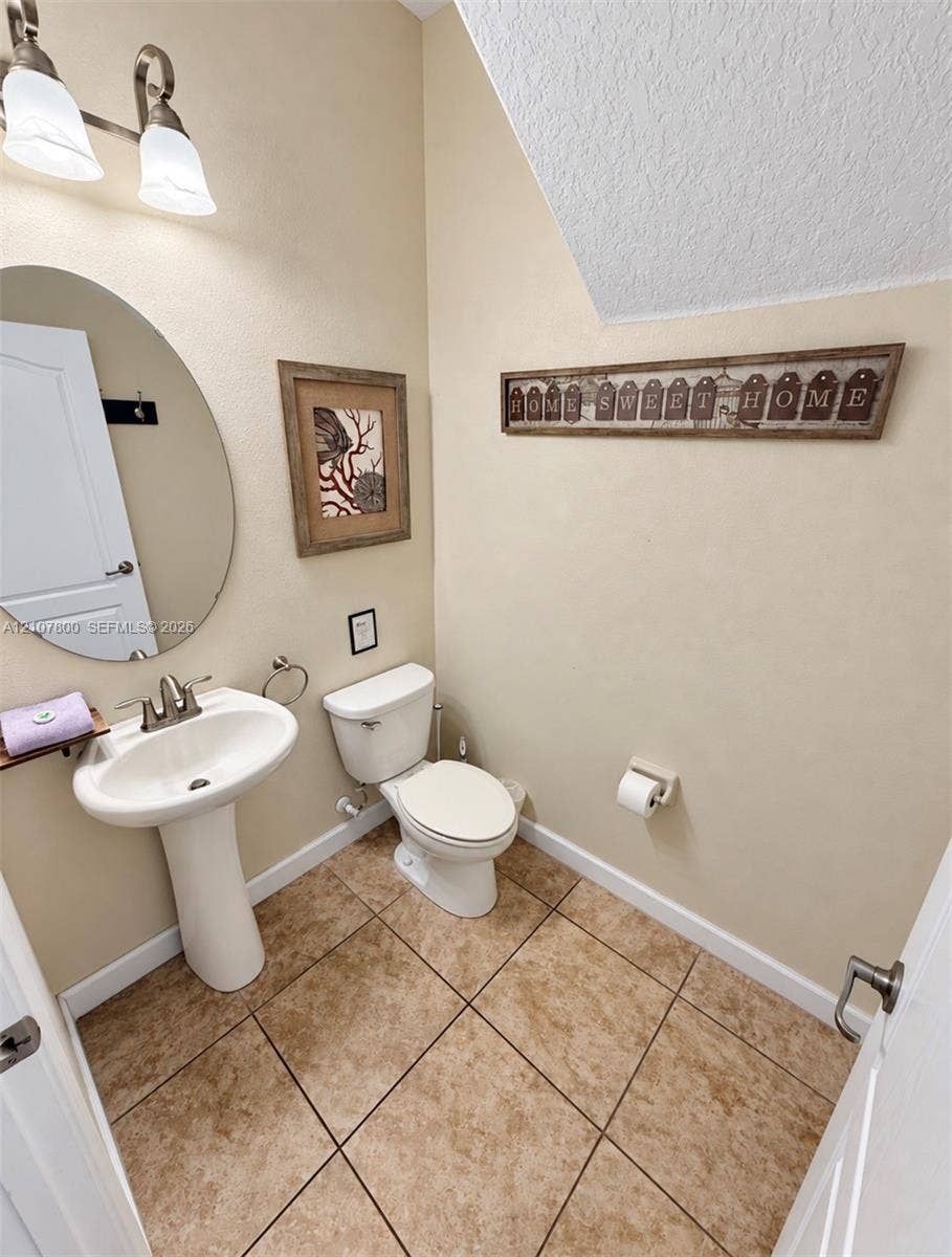1476 Moon Valley, Davenport, FL 33896 Pedestal sink with chrome faucet, oval wall-mounted mirror, two-light fixture with glass shades, and ceramic tile flooring