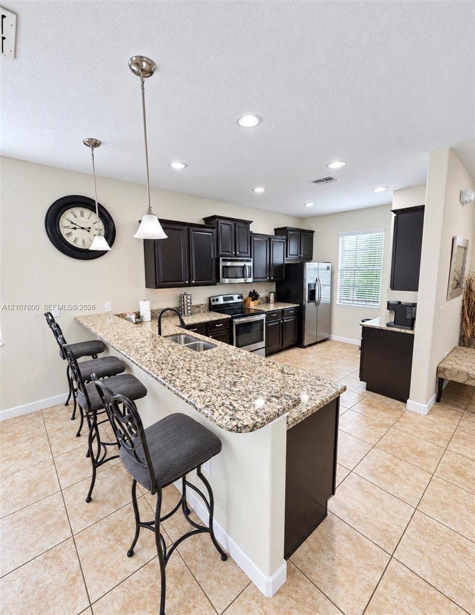 1476 Moon Valley, Davenport, FL 33896 Kitchen featuring dark cabinetry, expansive stone-finish countertops, stainless steel appliances, dual pendant lighting, and ceramic tile flooring