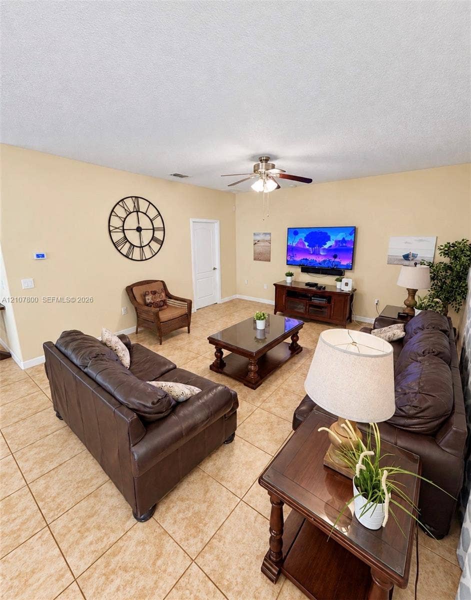 1476 Moon Valley, Davenport, FL 33896 Neutral-toned living space featuring large-format ceramic tile flooring, a central ceiling fan with integrated lighting, and a solid-core interior door