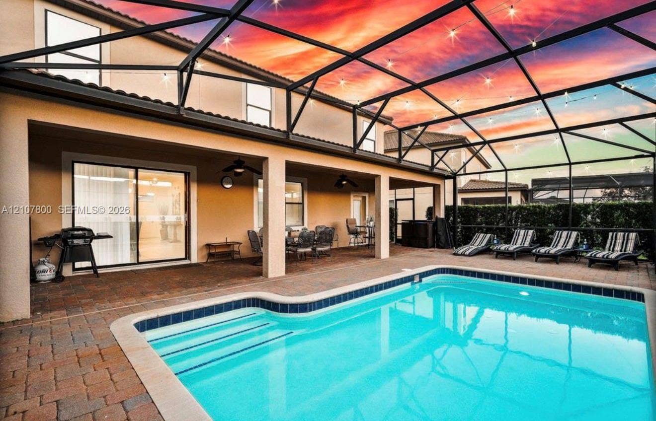 1476 Moon Valley, Davenport, FL 33896 Screened-in pool area featuring paver patio surfacing, integrated ceiling fans, and string lighting against a sunset backdrop