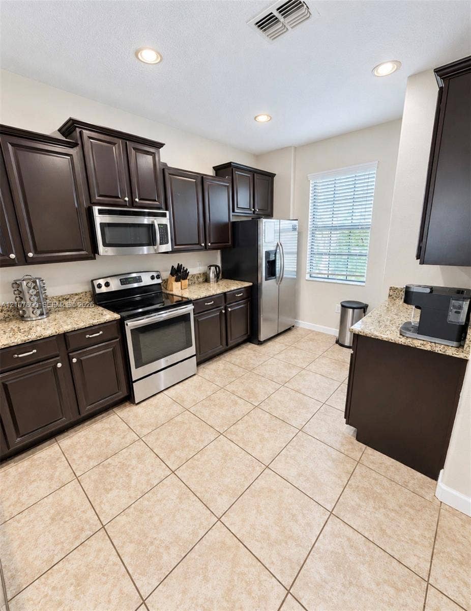1476 Moon Valley, Davenport, FL 33896 Kitchen featuring dark wood cabinetry, stone countertops, stainless steel appliances, and tiled flooring