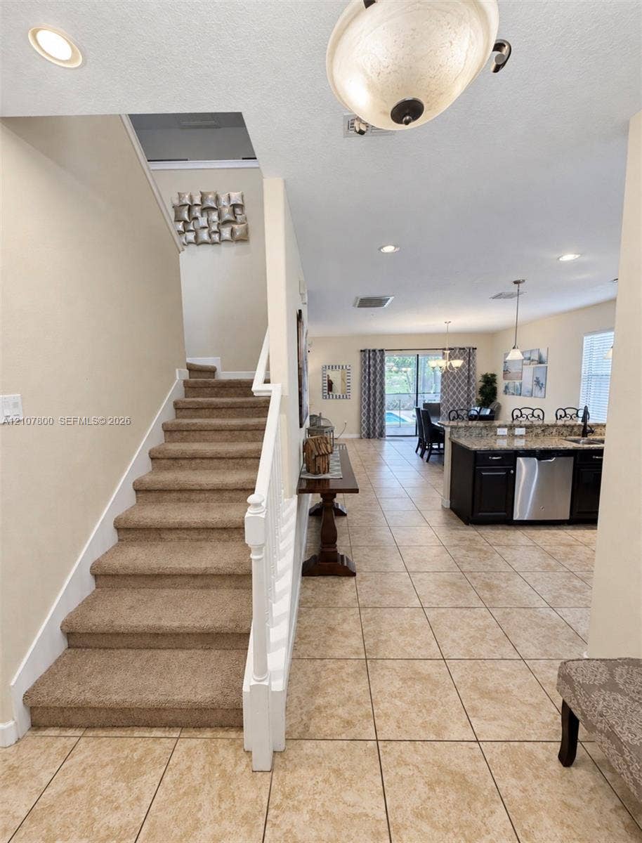1476 Moon Valley, Davenport, FL 33896 Carpeted staircase with white painted balustrade, tile flooring, kitchen featuring dark cabinetry and stainless steel appliances, and ceiling-mounted light fixtures