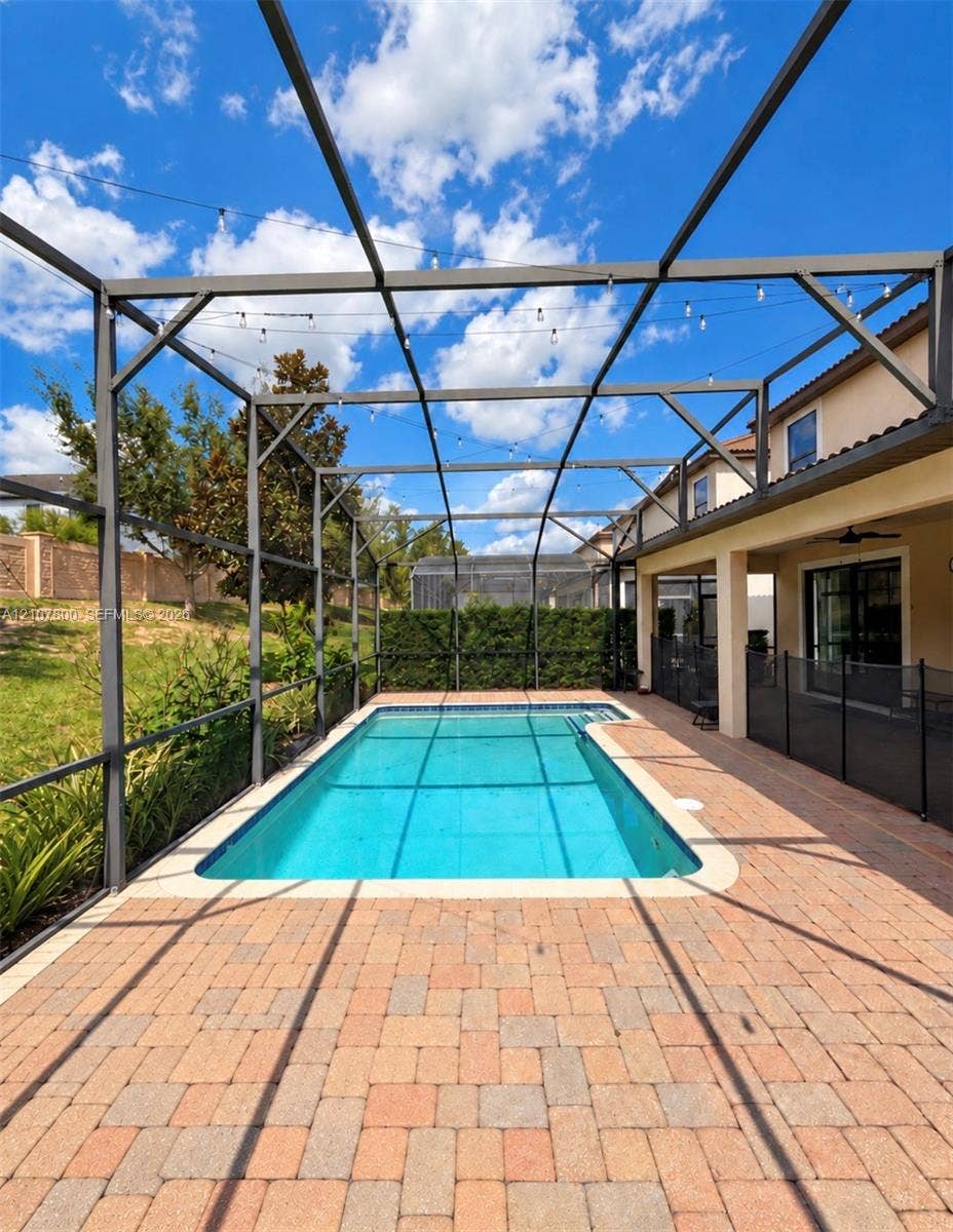 1476 Moon Valley, Davenport, FL 33896 In-ground swimming pool enclosed by a screen cage, featuring brick paver decking, a perimeter privacy hedge, and overhead string lighting