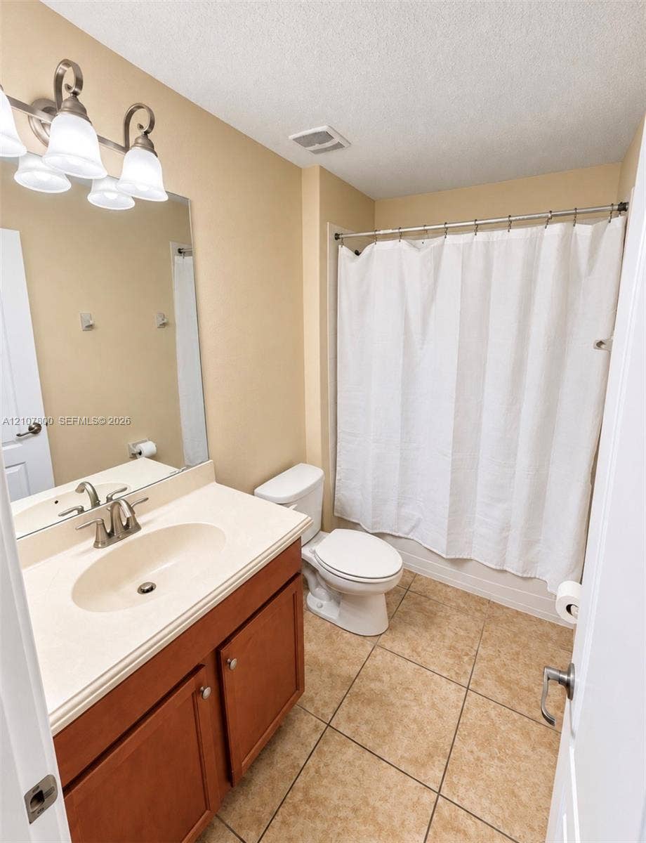 1476 Moon Valley, Davenport, FL 33896 Bathroom featuring a wood-toned vanity with an integrated sink, neutral stone-finish countertop, tiled flooring, and multi-bulb vanity lighting