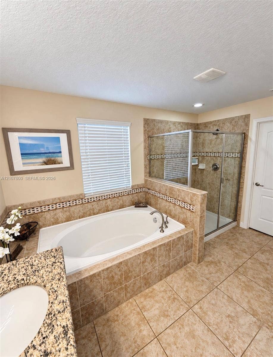 1476 Moon Valley, Davenport, FL 33896 Oval soaking tub with tiled surround, separate glass-enclosed shower, stone-finish countertop, and integrated ceramic sink