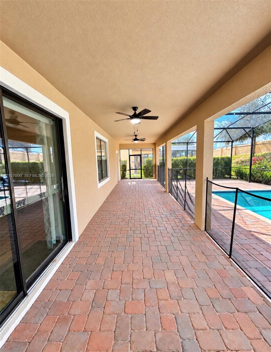 1476 Moon Valley, Davenport, FL 33896 Covered patio featuring brick-paver flooring, dual ceiling fans, sliding glass door access, and a screened-in pool enclosure