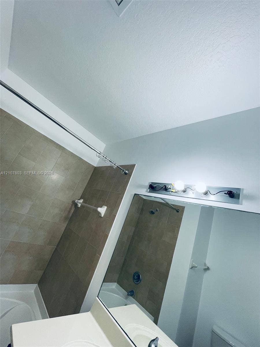 8620 NW 97th Avenue, #205, Doral, FL 33178 Bathroom featuring neutral wall tiling, a built-in tub, a large vanity mirror, and multi-bulb wall-mounted lighting