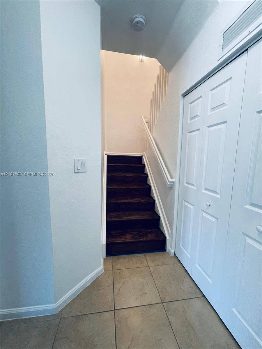8620 NW 97th Avenue, #205, Doral, FL 33178 Staircase featuring wood-finish treads, white painted handrails, large-format tile flooring, and a floor-to-ceiling closet with paneled double doors