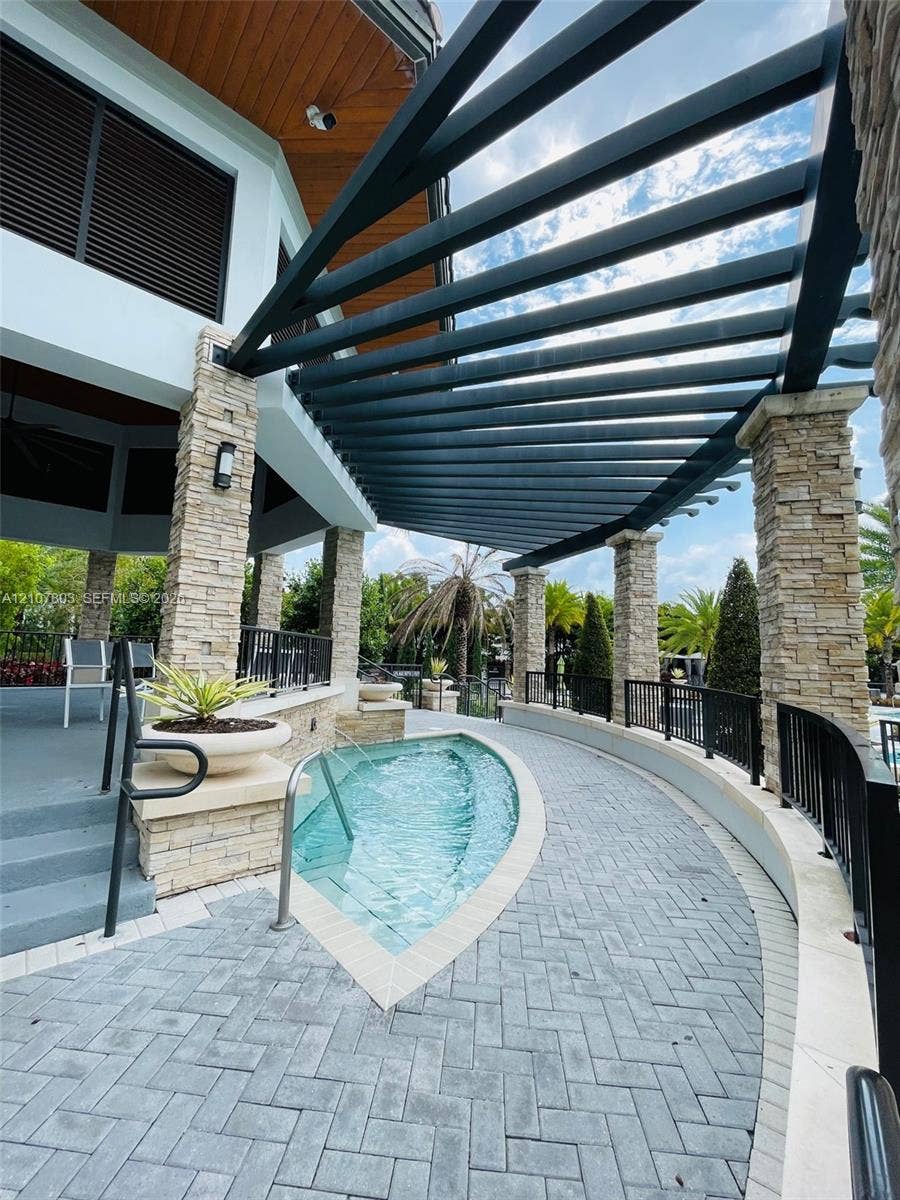 8620 NW 97th Avenue, #205, Doral, FL 33178 Custom outdoor space featuring a stone-columned pergola, curved pool with integrated entry stairs, paved herringbone patio, and wood-paneled ceiling details