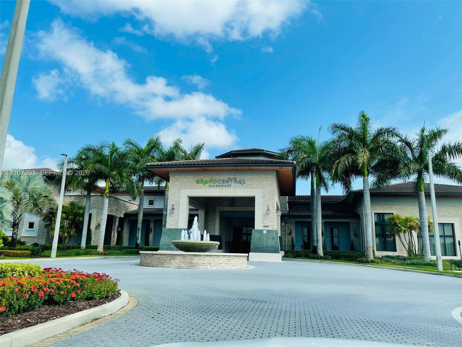 8620 NW 97th Avenue, #205, Doral, FL 33178 Clubhouse exterior featuring a stone-clad facade, covered porte-cochre, decorative water fountain, and mature palm trees