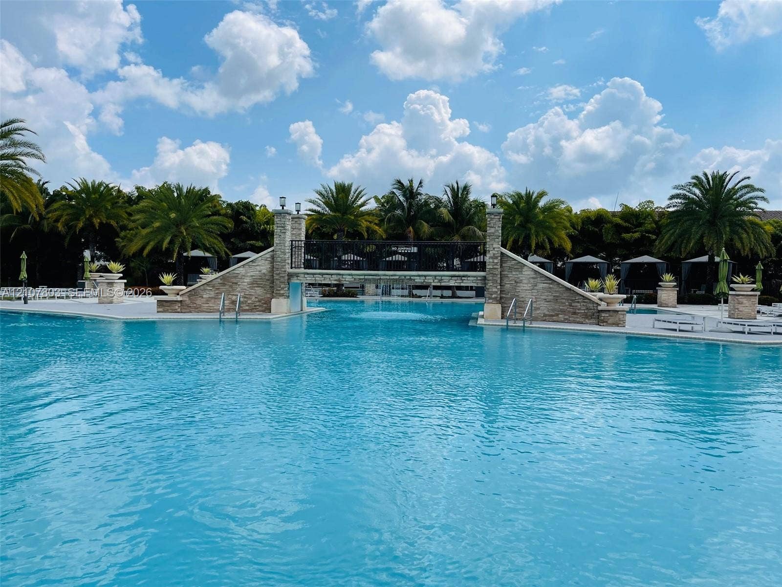 8620 NW 97th Avenue, #205, Doral, FL 33178 Swimming pool featuring a stone-clad pedestrian bridge, metal railings, integrated stone planters, and paved decking