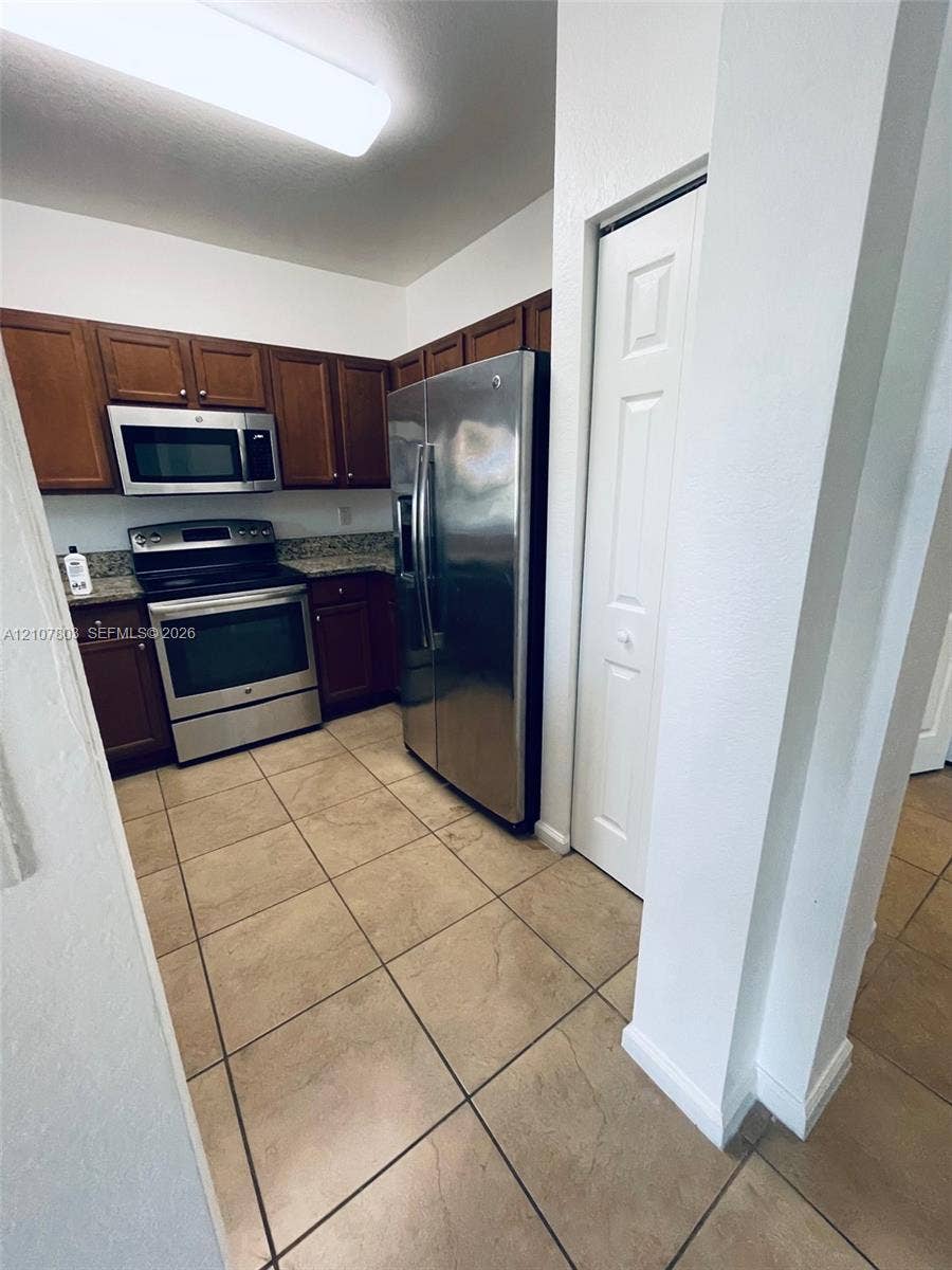 8620 NW 97th Avenue, #205, Doral, FL 33178 Kitchen featuring dark-toned cabinetry, stone-finish countertops, stainless steel appliances, ceramic tile flooring, and a floor-to-ceiling bi-fold door pantry