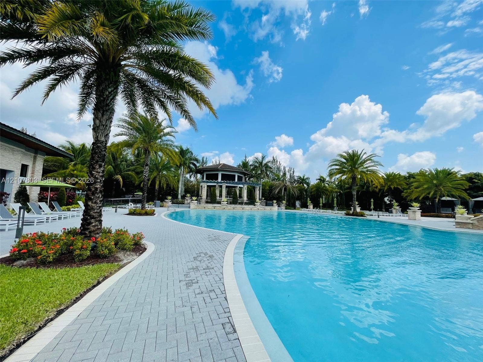 8620 NW 97th Avenue, #205, Doral, FL 33178 Curved swimming pool featuring a brick-paver deck, integrated gazebo, and mature palm landscaping