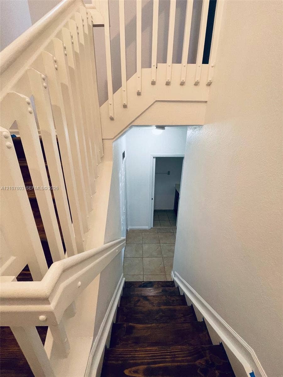 8620 NW 97th Avenue, #205, Doral, FL 33178 Staircase featuring stained wood treads, white-painted wood balusters, and a solid wood handrail with ceramic tile flooring at the base