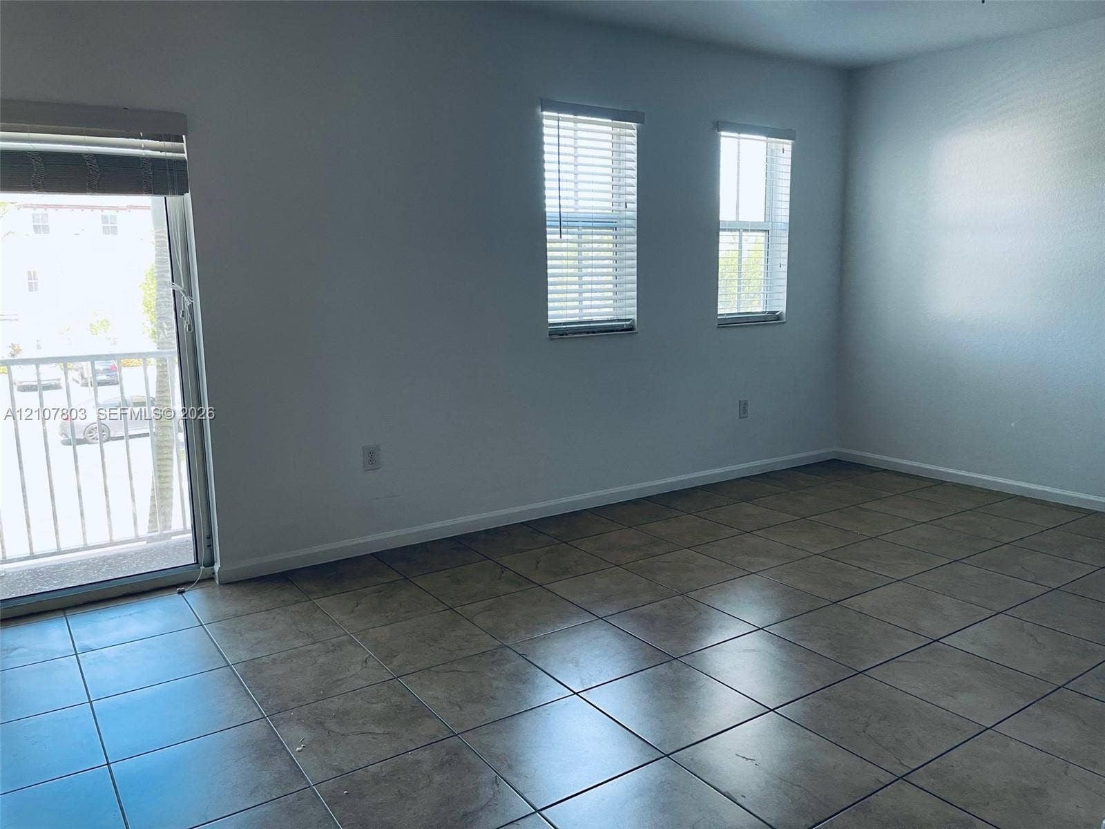 8620 NW 97th Avenue, #205, Doral, FL 33178 Interior space featuring ceramic tile flooring, two double-hung windows with horizontal blinds, and a sliding glass door with access to an exterior balcony