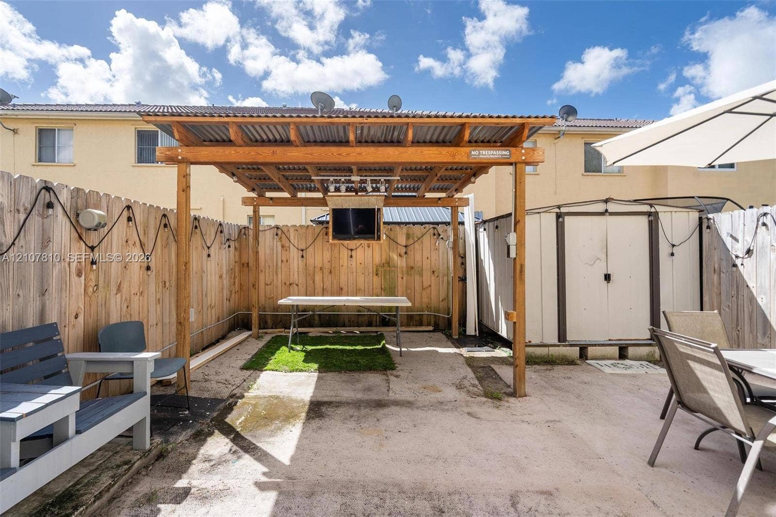 6940 NW 177th Street, #P105, Hialeah, Hialeah, FL 33015 Private rear courtyard featuring a covered timber-framed pergola with a corrugated metal roof, concrete patio, perimeter wood fencing, and a detached storage structure. Outdoor furniture, BBQ Grill and Outside TV stays.