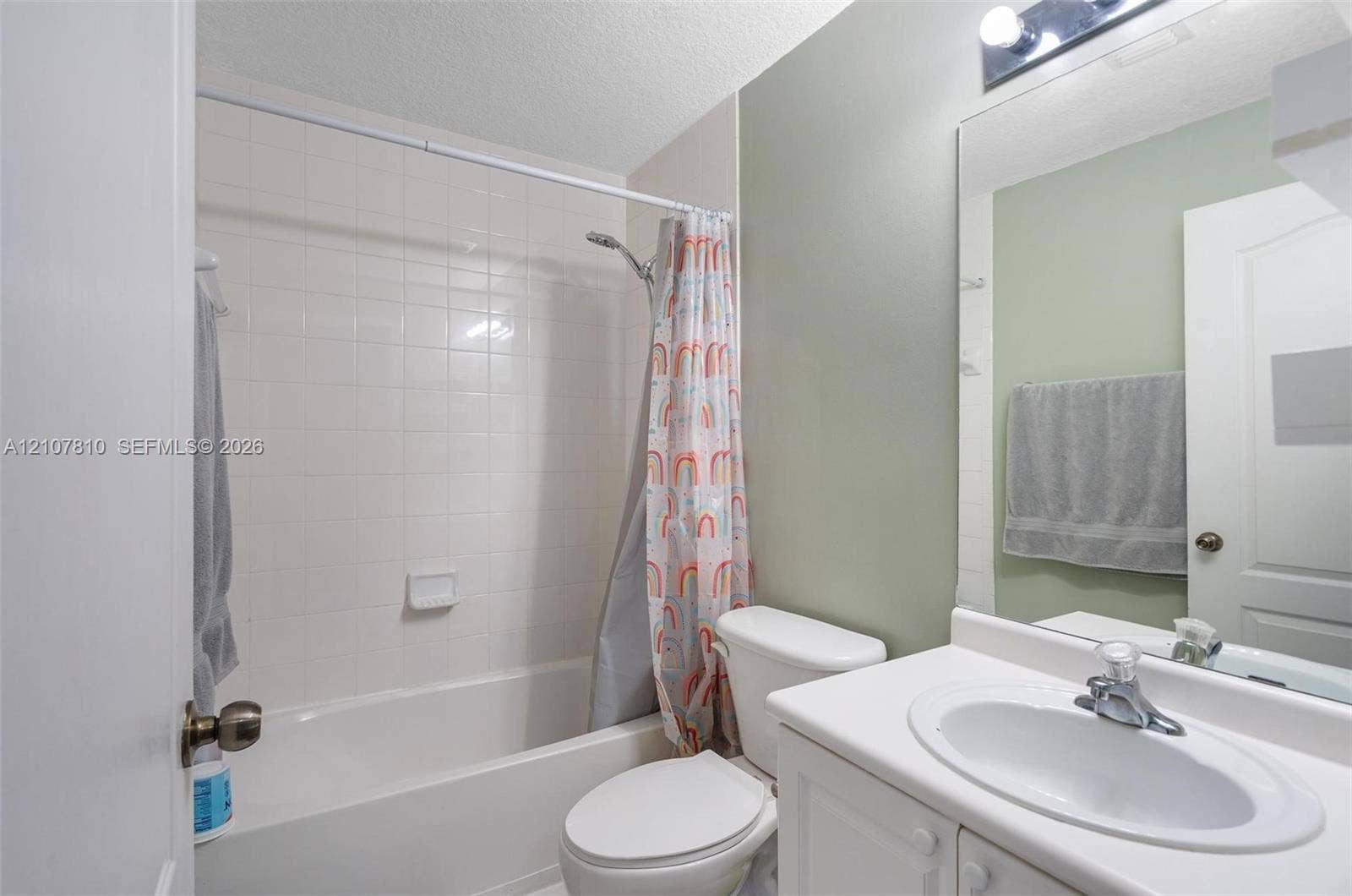 6940 NW 177th Street, #P105, Hialeah, Hialeah, FL 33015 Bathroom featuring a white vanity with an integrated sink, a full-width vanity mirror, a bathtub with a tiled surround, and a wall-mounted light fixture