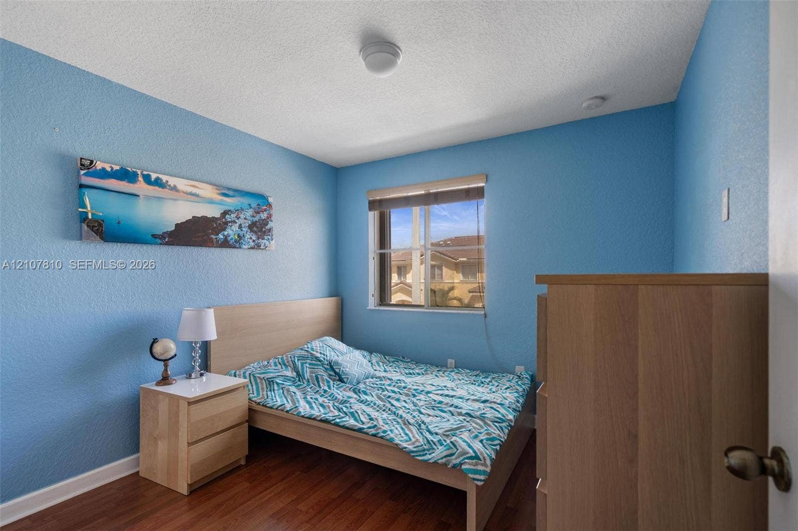 6940 NW 177th Street, #P105, Hialeah, Hialeah, FL 33015 Room featuring wood-finish flooring, textured walls, and a single-pane window with an integrated roller shade