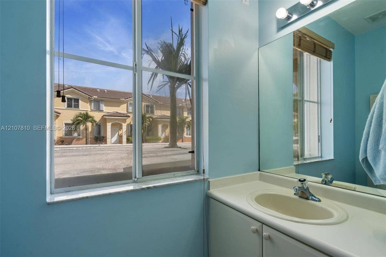 6940 NW 177th Street, #P105, Hialeah, Hialeah, FL 33015 Bathroom vanity featuring an integrated countertop and sink, large wall-mounted mirror, multi-bulb overhead lighting, and a window with exterior exposure