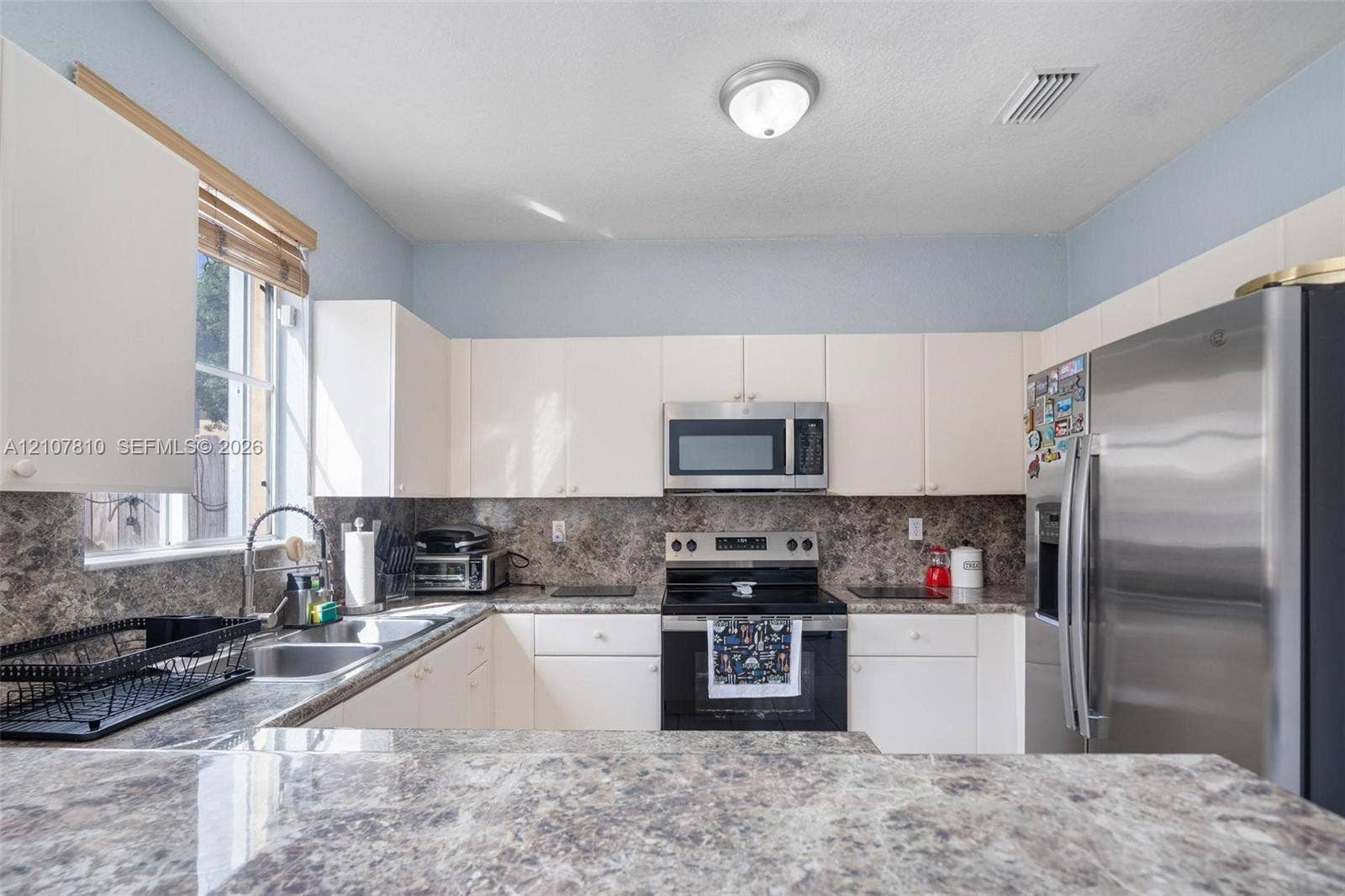 6940 NW 177th Street, #P105, Hialeah, Hialeah, FL 33015 Kitchen featuring white cabinetry, stone-patterned countertops, stainless steel refrigerator, over-the-range microwave, and dual-basin sink with a gooseneck faucet