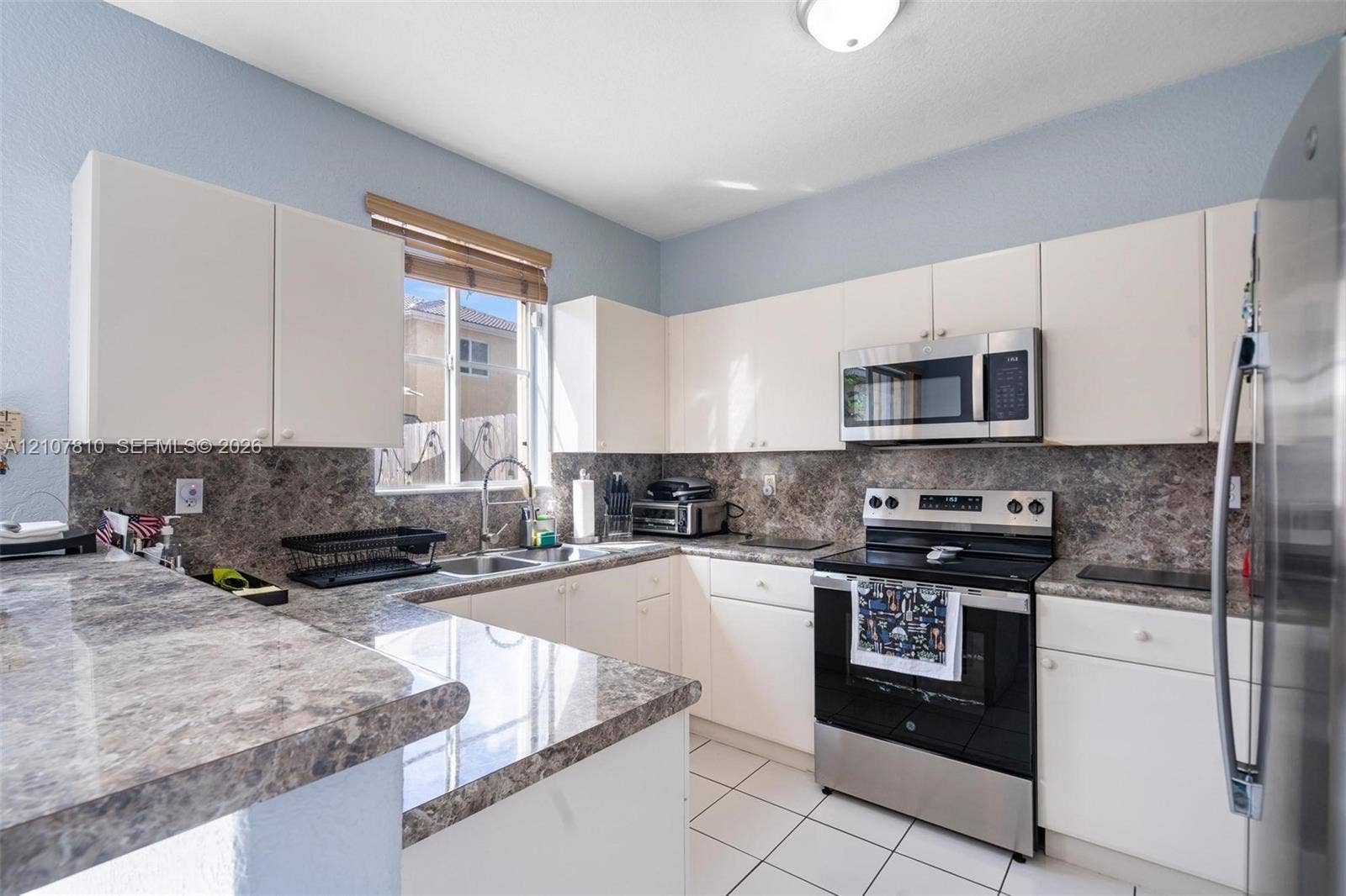 6940 NW 177th Street, #P105, Hialeah, Hialeah, FL 33015 Kitchen featuring white cabinetry, stone-patterned laminate countertops, full-height stone-patterned backsplash, stainless steel appliances, and tile flooring