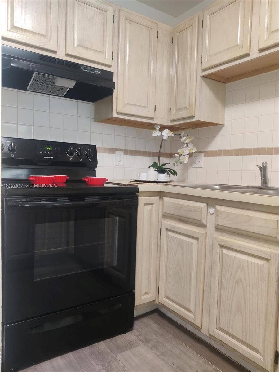 1705 Palm Cove Boulevard, #1-104, Delray Beach, Delray Beach, FL 33445 Kitchen featuring light-finish cabinetry, black freestanding range, matching black range hood, tiled backsplash, and wood-finish flooring