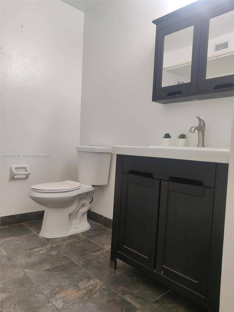 1705 Palm Cove Boulevard, #1-104, Delray Beach, Delray Beach, FL 33445 Dark-toned vanity with a rectangular sink, wall-mounted medicine cabinet, metal faucet, and stone-finish floor tiling