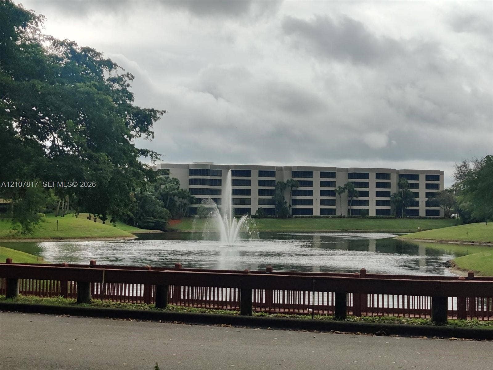 1705 Palm Cove Boulevard, #1-104, Delray Beach, Delray Beach, FL 33445 Multi-story building exterior featuring a central water fountain, landscaped grass slopes, and a perimeter railing