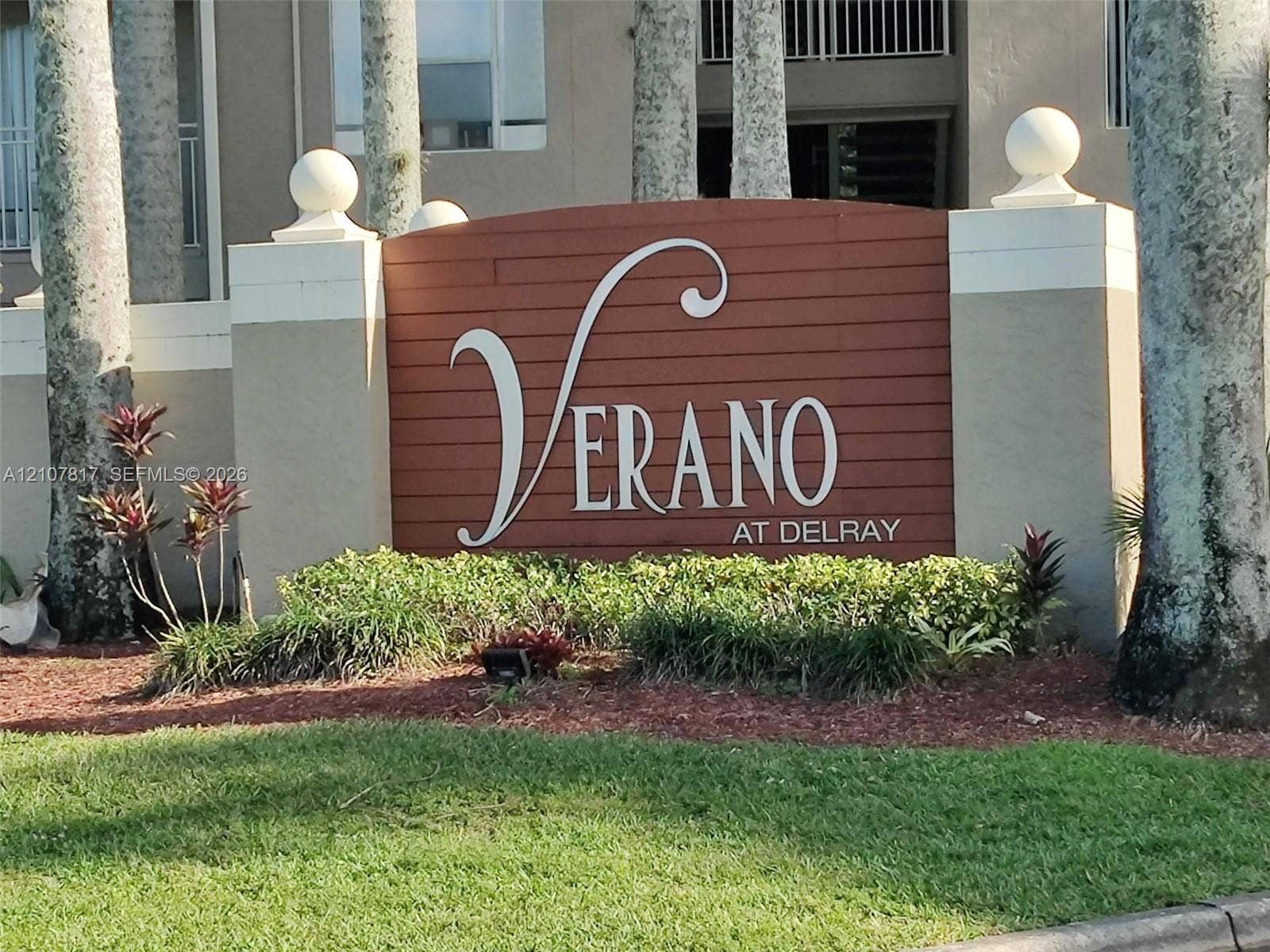 1705 Palm Cove Boulevard, #1-104, Delray Beach, Delray Beach, FL 33445 Community monument sign featuring horizontal wood-slat siding, decorative concrete pillars with ball finials, and professional landscaping