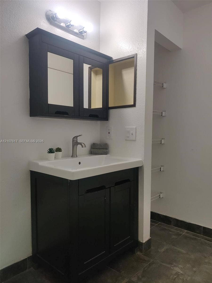 1705 Palm Cove Boulevard, #1-104, Delray Beach, Delray Beach, FL 33445 Dark wood-finish vanity with an integrated basin, wall-mounted mirrored medicine cabinet, single-handle brushed metal faucet, and built-in wire shelving