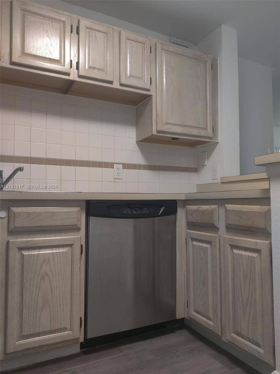 1705 Palm Cove Boulevard, #1-104, Delray Beach, Delray Beach, FL 33445 Kitchen featuring light-finish wood cabinetry, stainless steel dishwasher, square tile backsplash with decorative accent inlay, and wood-finish flooring