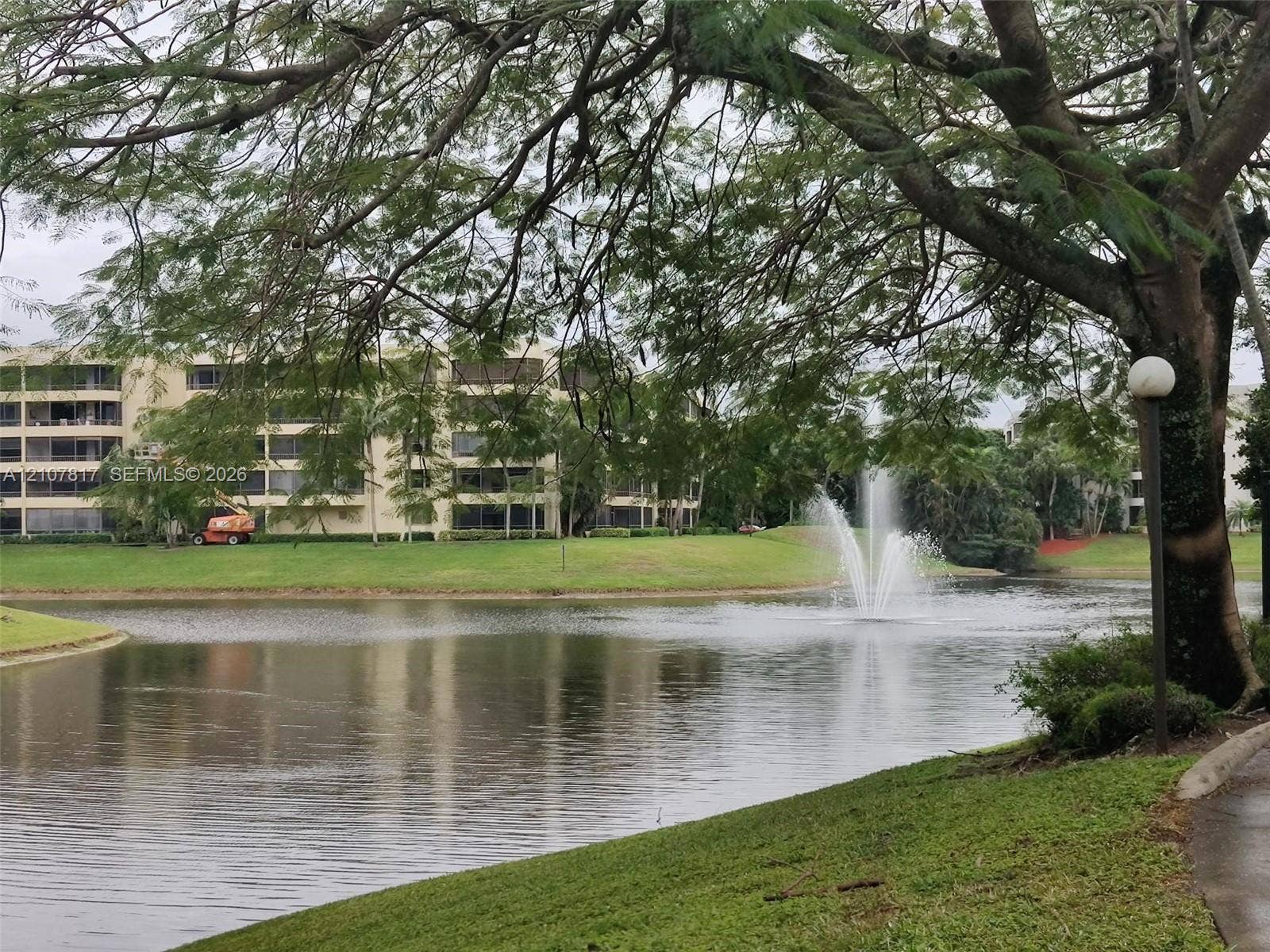 1705 Palm Cove Boulevard, #1-104, Delray Beach, Delray Beach, FL 33445 Waterfront setting featuring a central fountain, manicured lawn, mature trees, and paved walkway