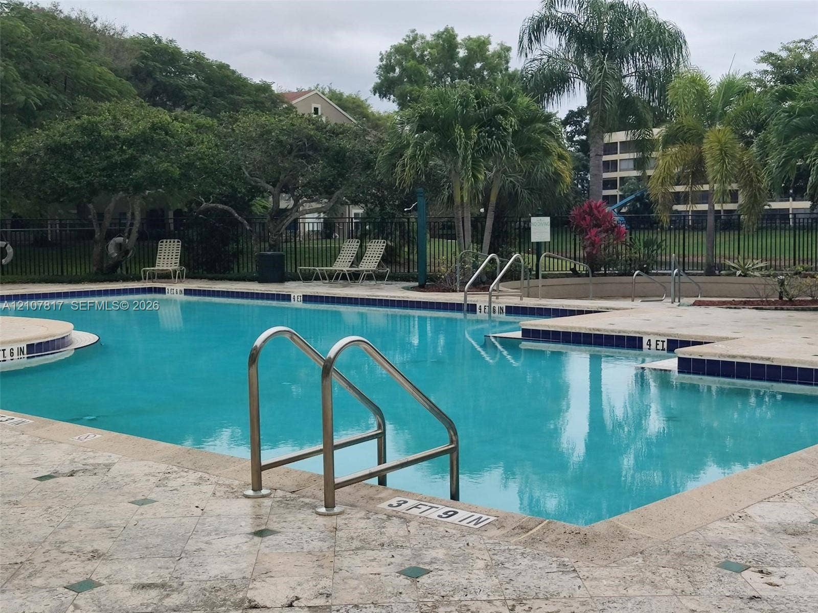 1705 Palm Cove Boulevard, #1-104, Delray Beach, Delray Beach, FL 33445 Swimming pool featuring tile trim, stone paver decking, integrated handrails, and mature landscaping