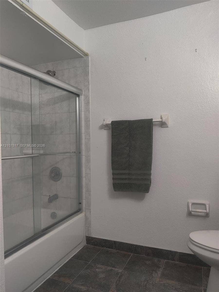 1705 Palm Cove Boulevard, #1-104, Delray Beach, Delray Beach, FL 33445 Shower-tub combination featuring a sliding glass enclosure, light-toned wall tile surround, dark slate-finish flooring, and chrome-finish plumbing fixtures