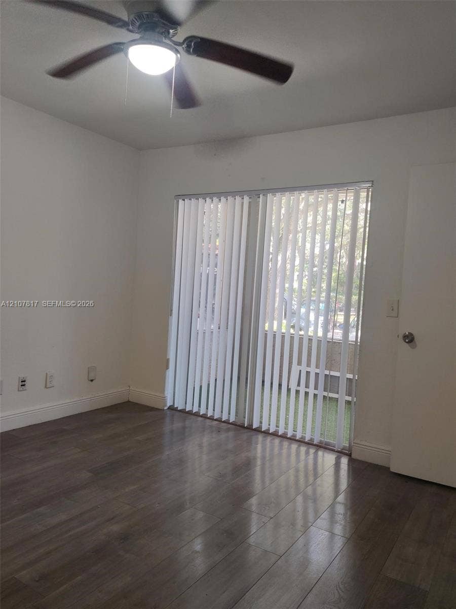 1705 Palm Cove Boulevard, #1-104, Delray Beach, Delray Beach, FL 33445 Interior space featuring wood-finish flooring, a ceiling fan with integrated light fixture, and vertical window blinds covering a sliding glass door