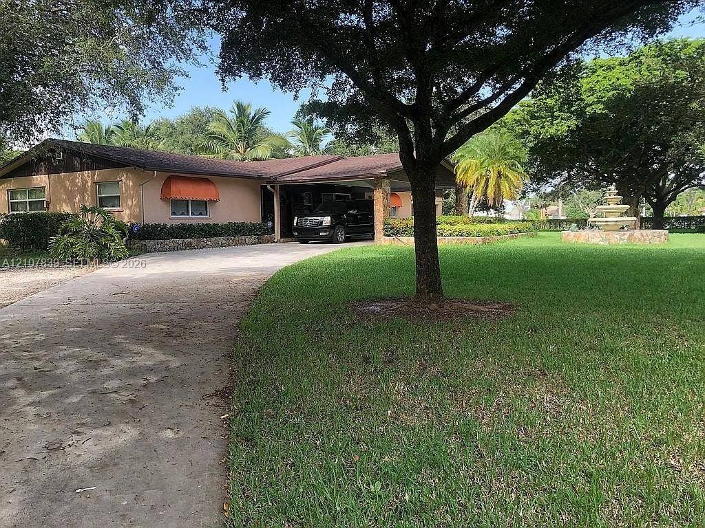 12105 NW 23rd Court, Plantation, FL 33323 Single-story exterior featuring a stone-clad portico, concrete driveway, stone tiered fountain, and mature landscaping