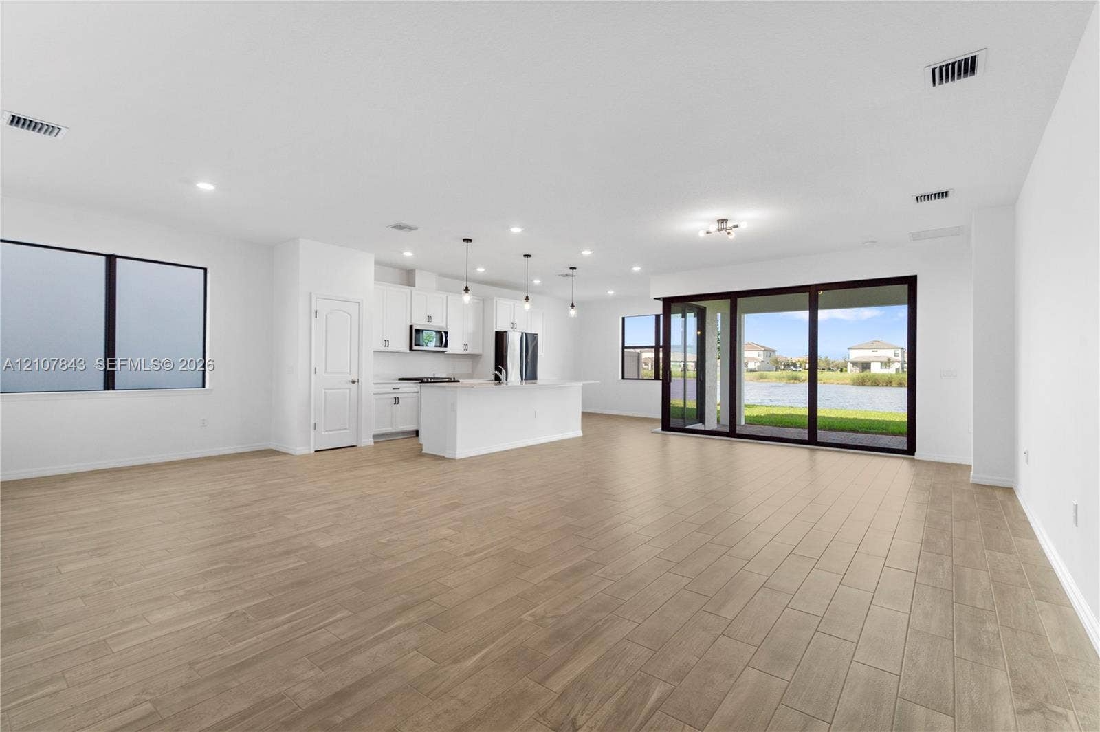 4949 Blistering Way, Lake Worth, FL 33467 Open-concept space featuring wood-finish tile flooring, white cabinetry, a center kitchen island, recessed lighting, and multi-panel sliding glass doors