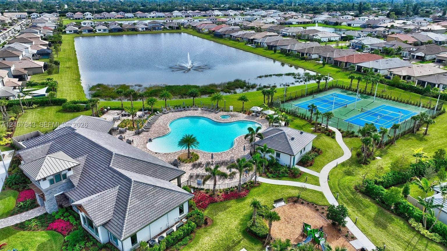 4949 Blistering Way, Lake Worth, FL 33467 Community amenities featuring a resort-style swimming pool, two tennis courts, and a large lake with a central fountain