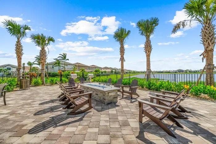 4949 Blistering Way, Lake Worth, FL 33467 Paver patio featuring a stone-clad linear fire pit, metal perimeter fencing, and mature palm trees overlooking a waterfront