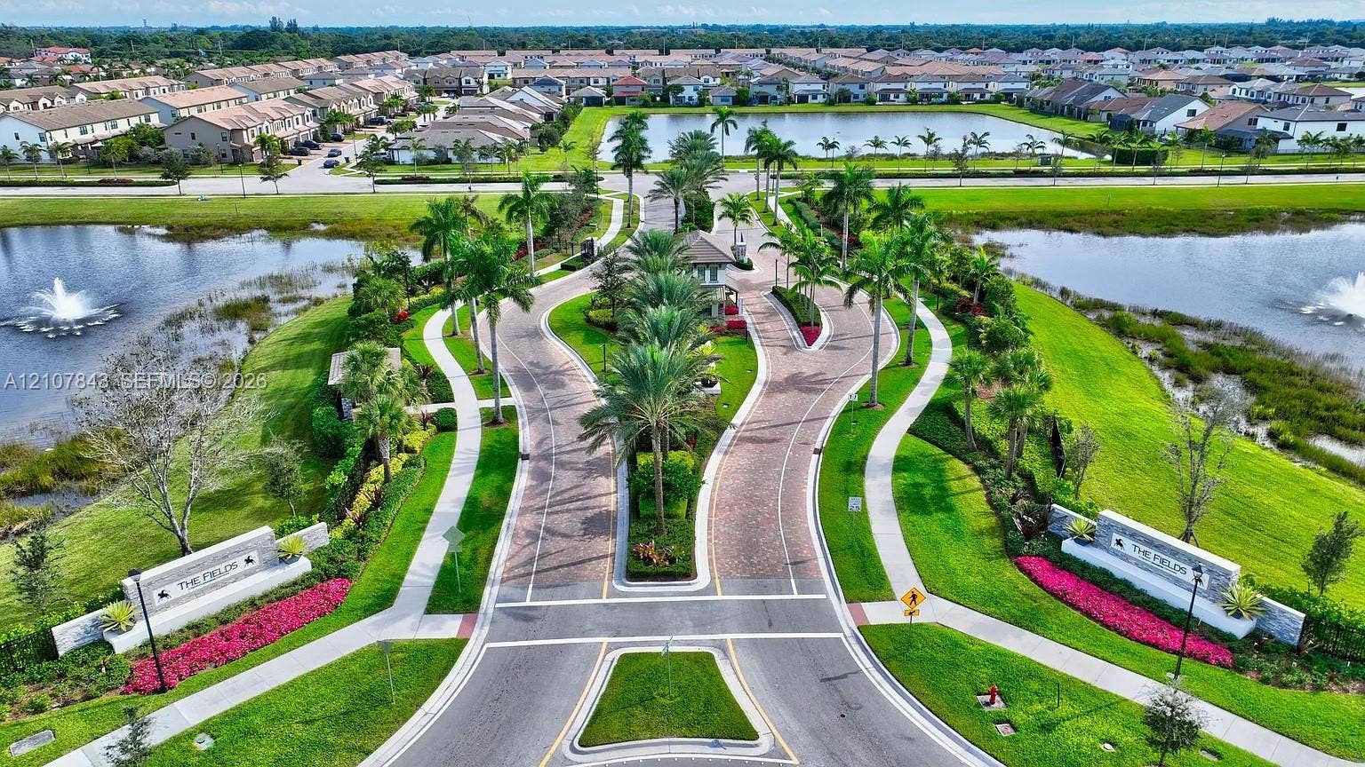 4949 Blistering Way, Lake Worth, FL 33467 Gated community entrance featuring paver-stone roadways, manicured landscaping with mature palms, ornamental stone signage, and central water features