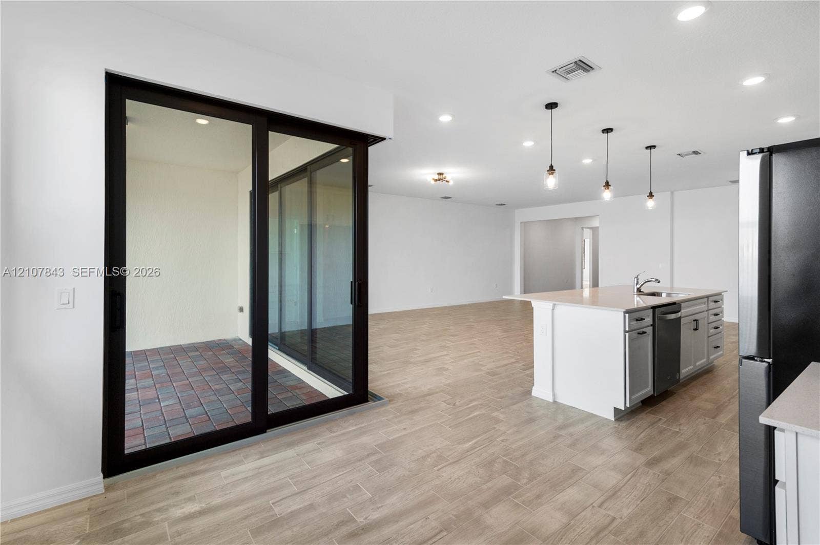 4949 Blistering Way, Lake Worth, FL 33467 Open-concept interior featuring wood-finish flooring, a kitchen island with light cabinetry and solid-surface countertops, recessed lighting, pendant light fixtures, and a large multi-panel sliding glass door leading to a paver patio
