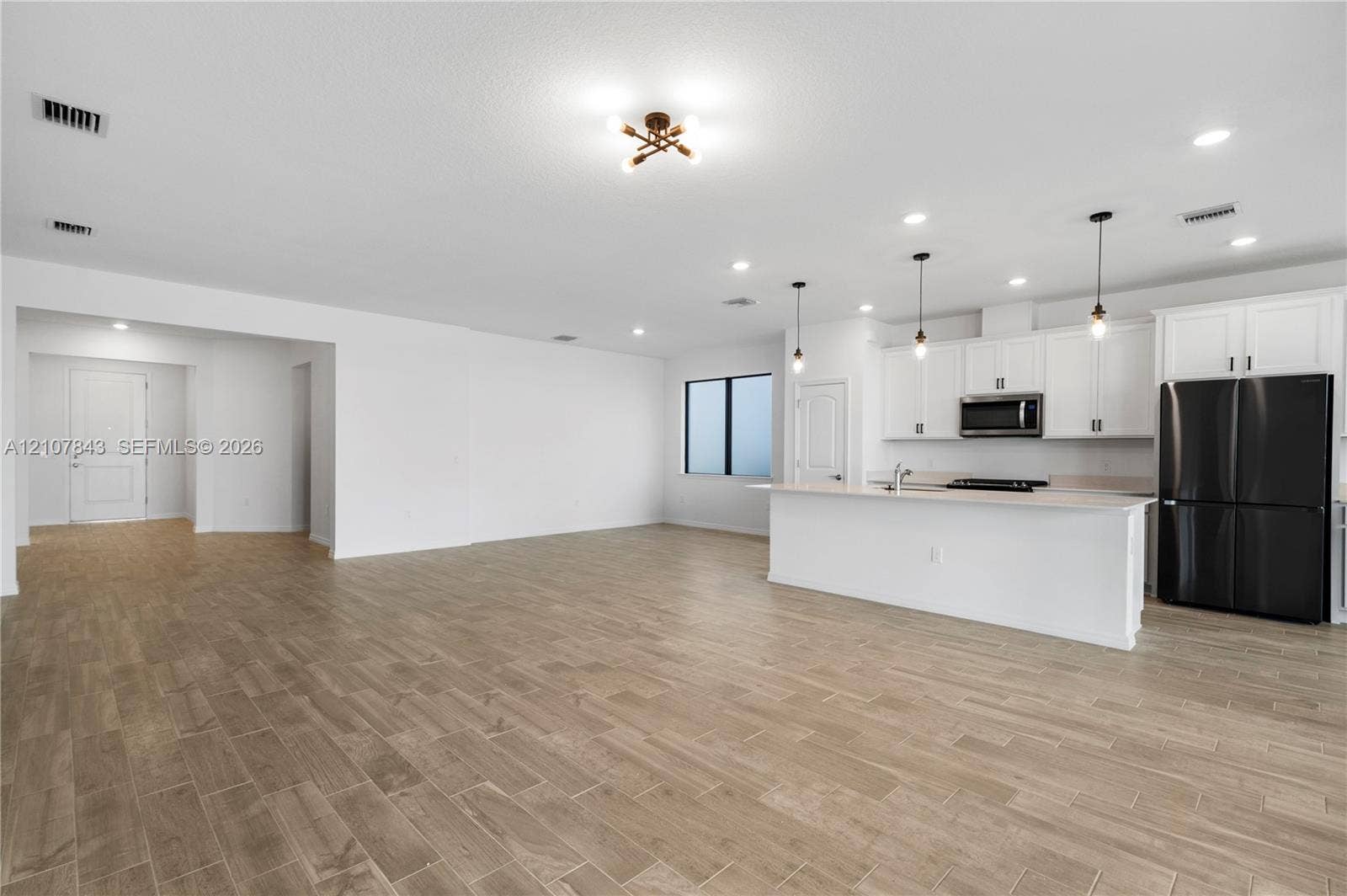 4949 Blistering Way, Lake Worth, FL 33467 Open-concept interior featuring wood-finish tile flooring, white cabinetry, a center island with pendant lighting, and stainless steel appliances