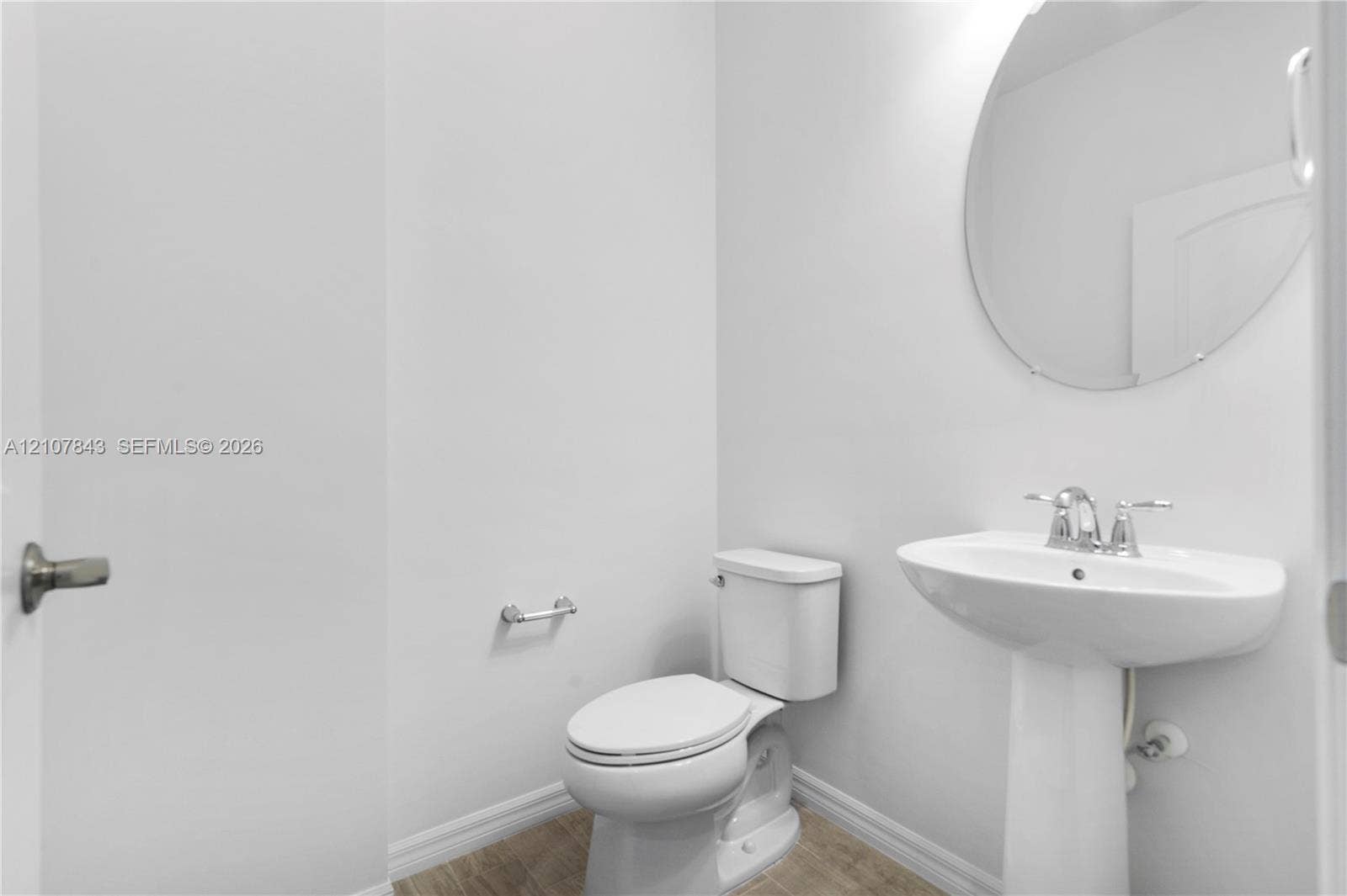 4949 Blistering Way, Lake Worth, FL 33467 White pedestal sink with chrome faucet, circular frameless mirror, and neutral tone flooring