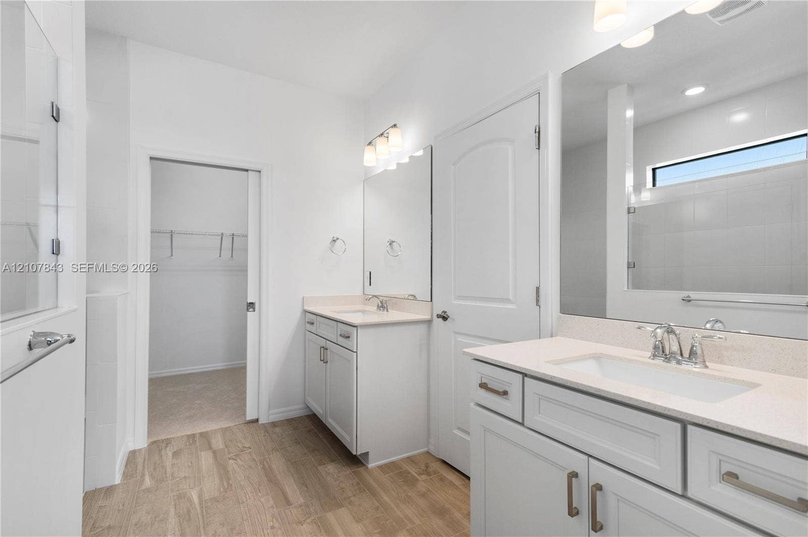 4949 Blistering Way, Lake Worth, FL 33467 Dual vanities with solid-surface countertops, wood-finish flooring, large wall-mounted mirrors, and an interior walk-in closet with built-in shelving