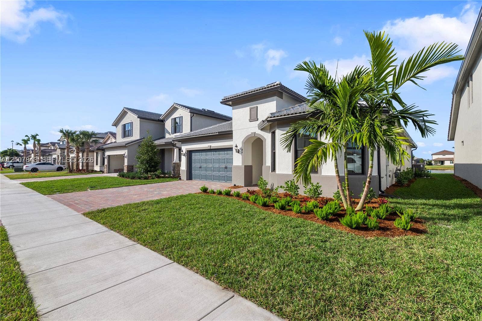 4949 Blistering Way, Lake Worth, FL 33467 Stucco exterior with a multi-gabled tile roof, paver driveway, attached two-car garage, and landscaped front yard