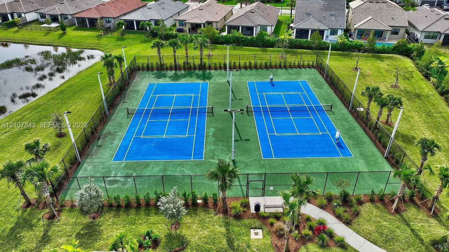 4949 Blistering Way, Lake Worth, FL 33467 Dual tennis courts featuring perimeter fencing, high-mast lighting, manicured landscaping, and a paved walkway