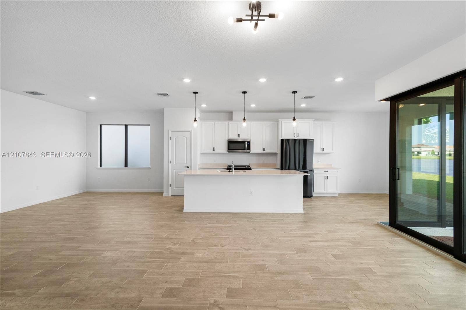 4949 Blistering Way, Lake Worth, FL 33467 Kitchen featuring white cabinetry, center island, integrated black appliances, wood-finish flooring, and sliding glass patio doors
