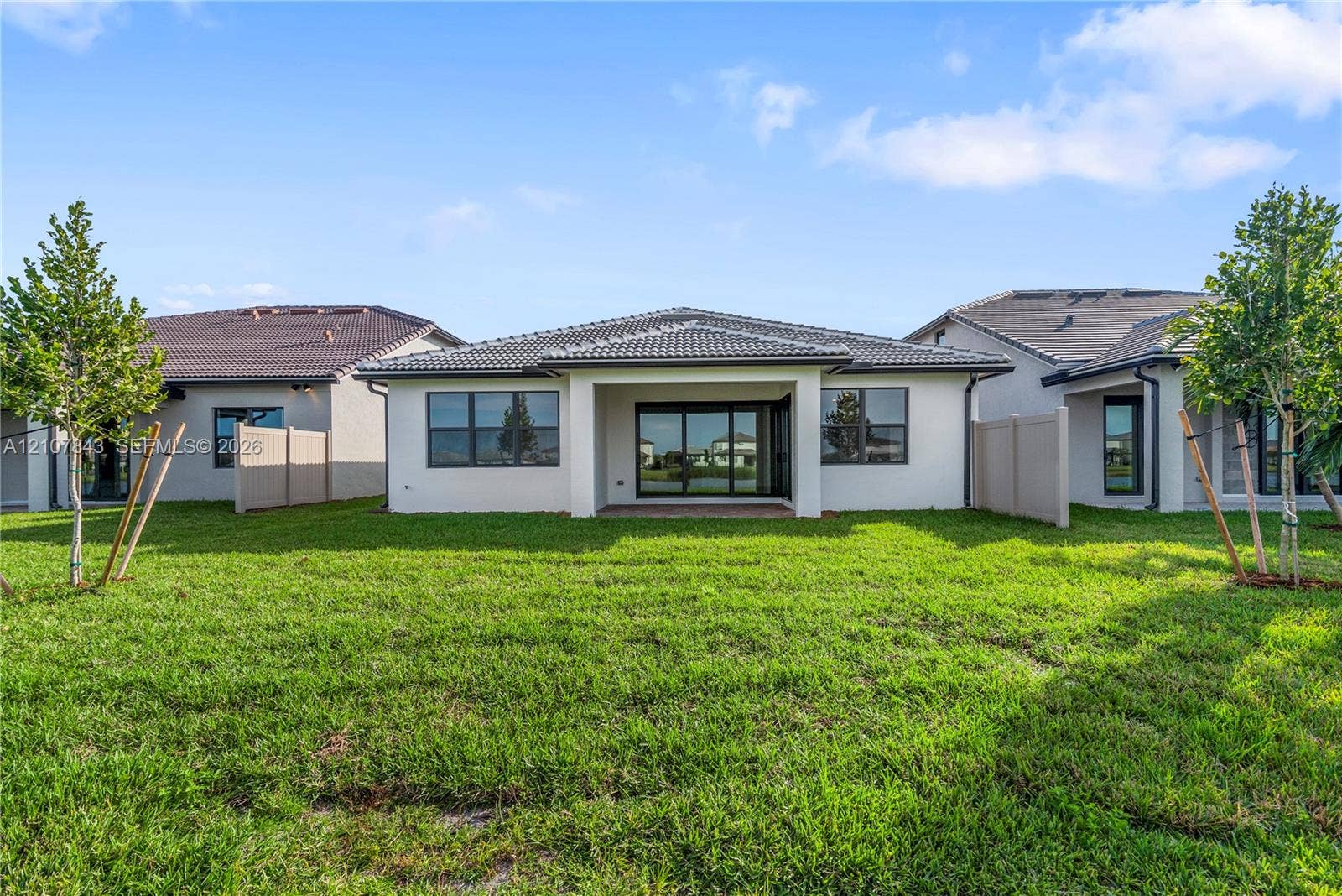 4949 Blistering Way, Lake Worth, FL 33467 Rear exterior featuring a covered patio, neutral stucco siding, a tiled roof, and an expansive grass lawn