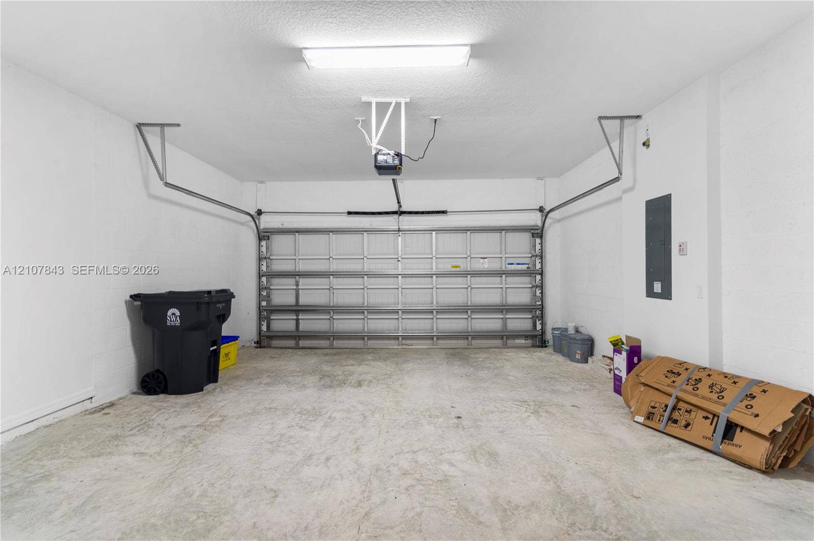 4949 Blistering Way, Lake Worth, FL 33467 Enclosed two-car garage featuring finished white walls, a metal sectional door, overhead lighting, and concrete flooring
