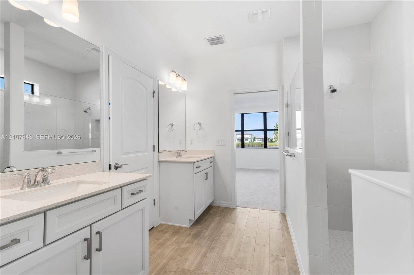 4949 Blistering Way, Lake Worth, FL 33467 Bathroom featuring dual white cabinetry with stone-surface countertops, wood-finish flooring, full-width vanity mirrors, and a glass-enclosed shower